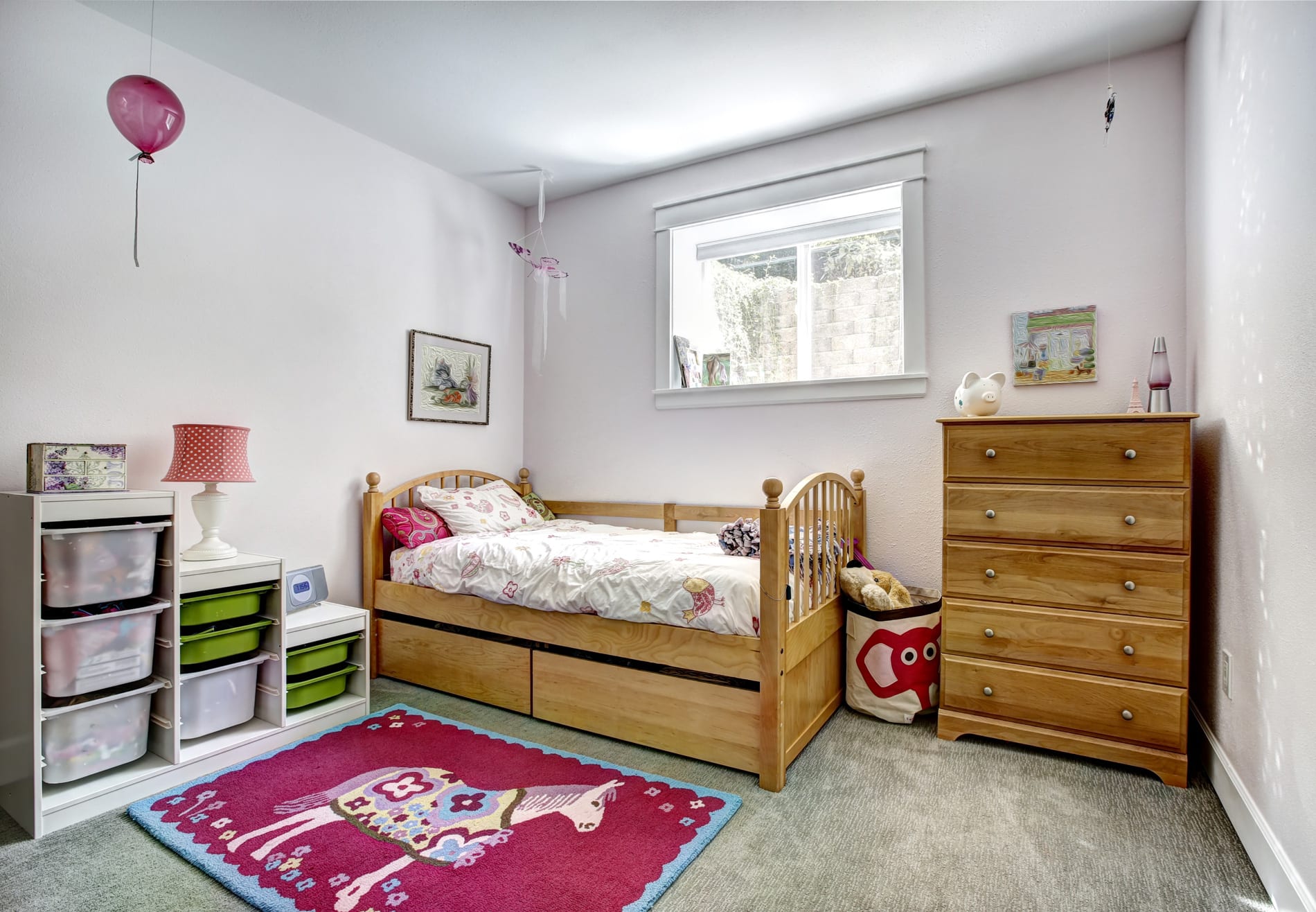 A cozy small bedroom featuring a bed, dresser, and a pink rug, designed by a Utah basement builder for optimal space use.