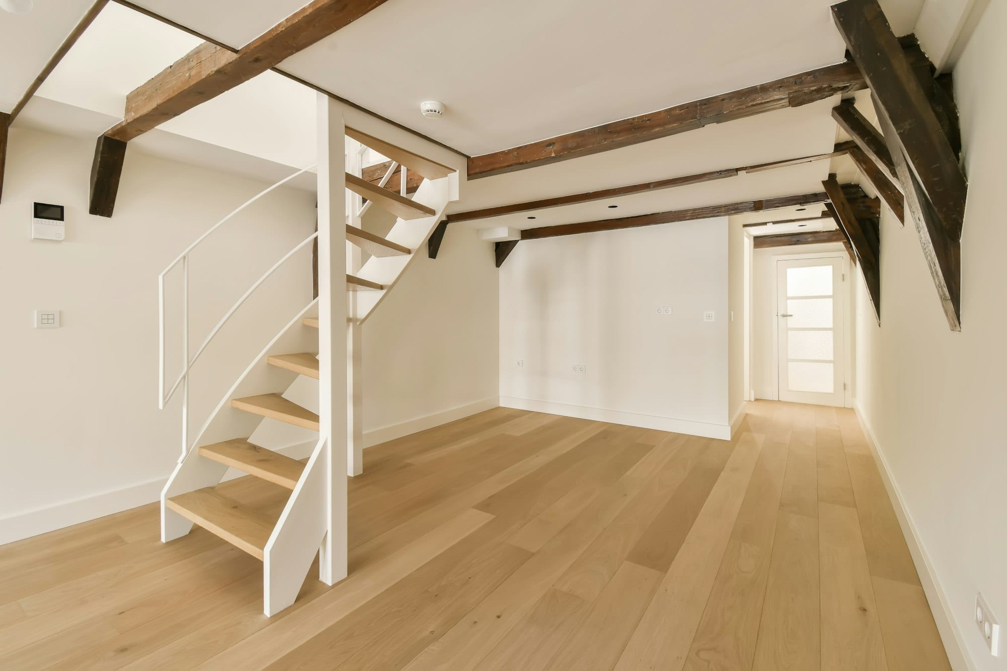  A white staircase in an empty room featuring wooden beams, showcasing a modern design by a Utah basement builder.