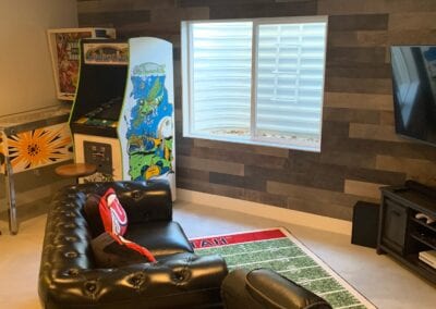 A cozy living room featuring a couch, television, and an arcade game, designed by a Utah basement builder for gaming enjoyment.