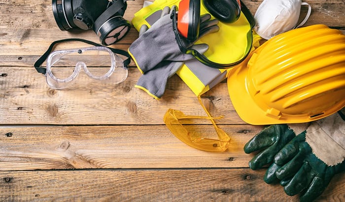 Safety Equipment For Basement Construction Displayed On A Wooden Table|A man in a hard hat and vest inspects electrical equipment in a basement construction site|A man in a hard hat holding a blueprint