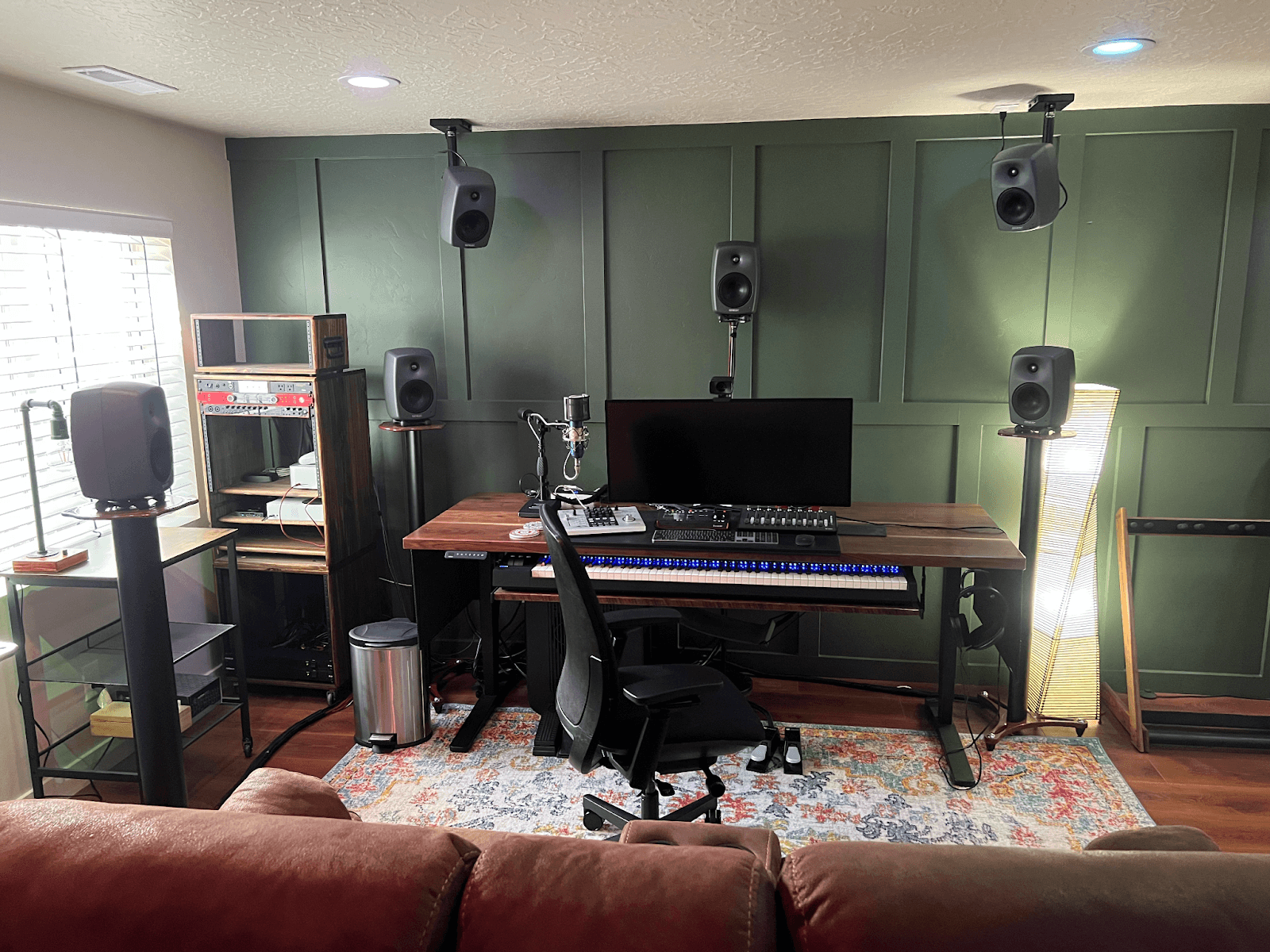 A small basement studio showcasing a desk, speakers, and a couch, ideal for work and leisure in a remodeled space.