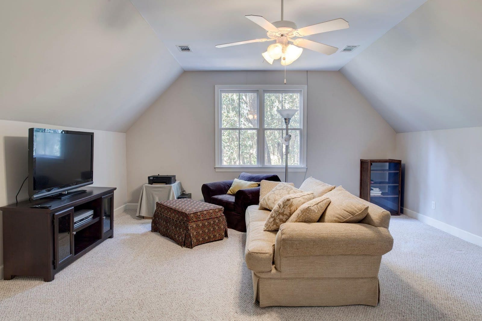 A snug attic room with a couch, television, and ceiling fan, perfect for relaxation