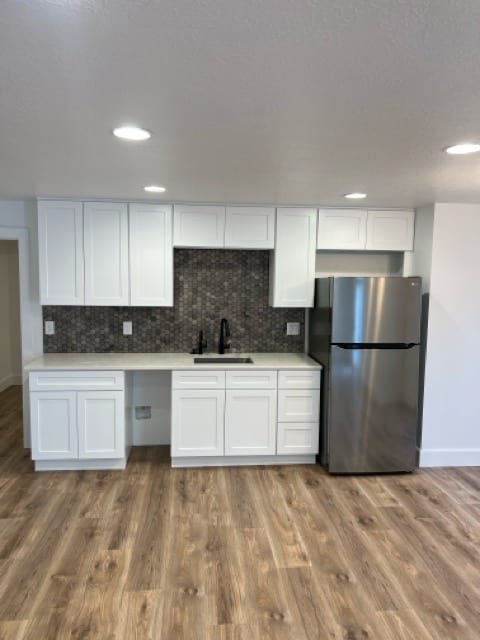 Modern kitchenette with white shaker cabinets, stainless steel fridge, black faucet, hexagon tile backsplash, light wood-look flooring, and recessed lighting. Clean and bright.