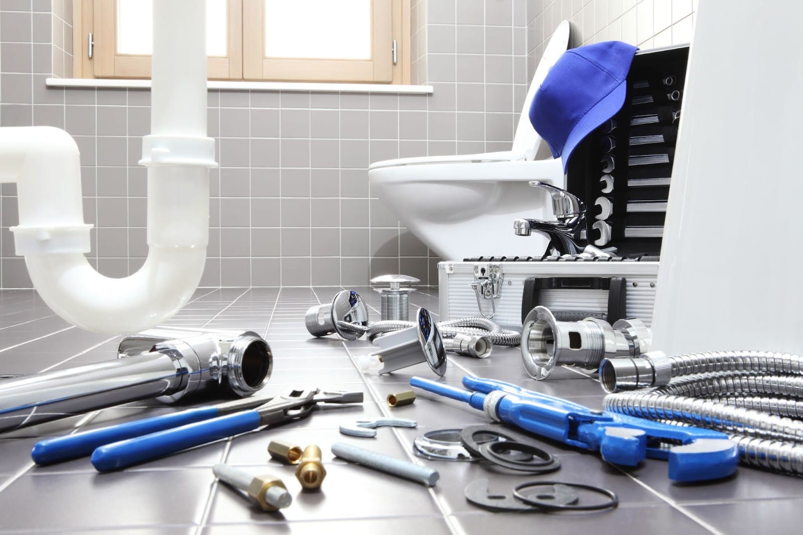Plumbing tools, including wrenches and pipes, are laid out on a tiled bathroom floor in front of a white toilet during a renovation or repair.